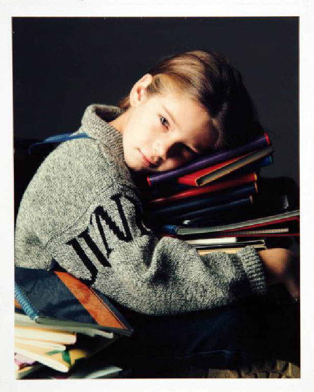 Campagna pubblicitaria per Trussardi Junior - bambina indossa un maglione grigio melange - appoggia il capo su una pila di quaderni