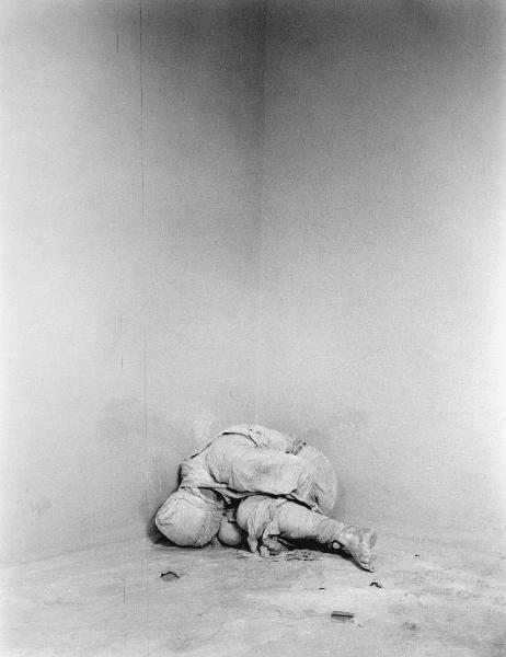 Ana. Performance - Uomo vestito con bende nell'angolo di una stanza vuota - Macchie sul pavimento