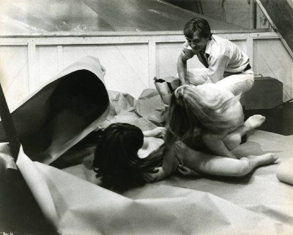 Ritratto. Foto di scena del film Blow-Up. David Hammings guarda due modelle nude a terra. Set fotografico
