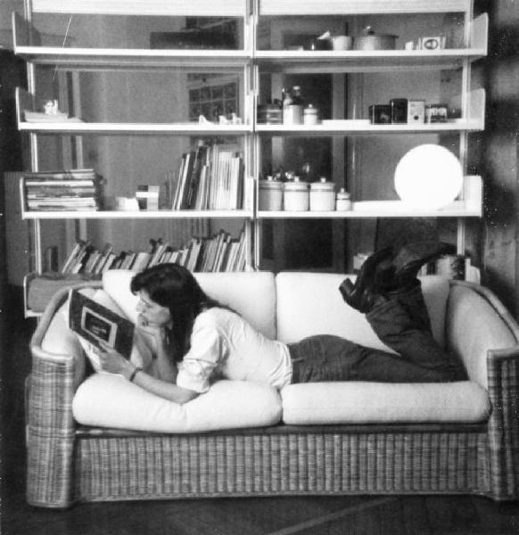 Ragazzo legge una rivista sdraiato sul divano mentre osserva una foto.