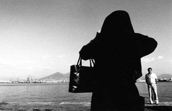 Napoli. Donna in abito nero con uomo in riva al mare