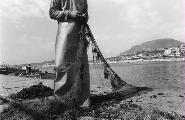 Pescatore ripara la rete in riva al mare