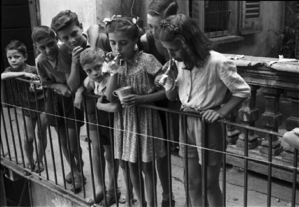 Milano. Bambine e bambini affacciati ad un balcone - due bambine fanno le bolle di sapone