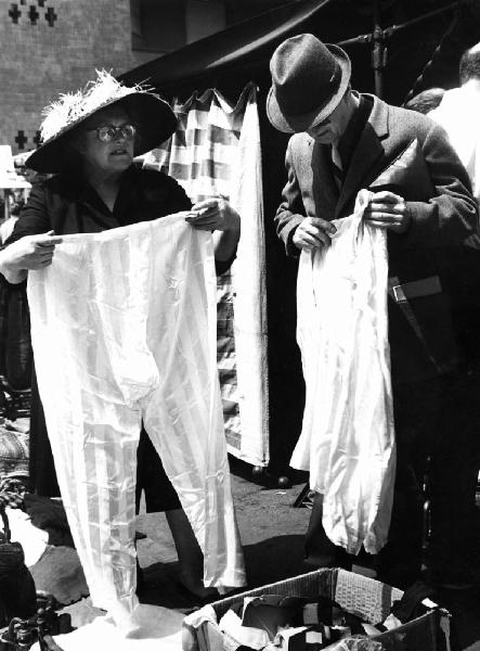Fiera di Sinigaglia. Milano - Mercatino - Donna ambulante con cappello di paglia e pantaloni in mano - Uomo con abito in mano