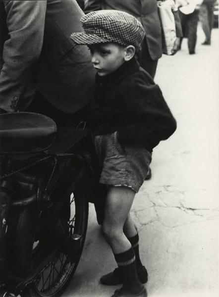 Fiera di Sinigaglia. Milano - Mercatino - Ritratto infantile - Bambino con cappello, pantaloncini, mani in tasca - Motocicletta