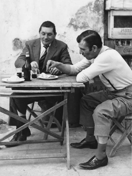 Osteria: Bocce. Italia del Nord - Osteria - Ritratto maschile - Uomini a un tavolo - Pranzo: piatto con cibo, bottiglia di vino, bicchieri