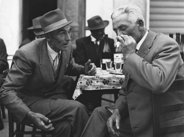 Osteria: Bocce. Italia del Nord - Osteria - Ritratto di gruppo - Due anziani in primo piano - Sigaretta, fumo - Cappello - Bottiglie di vino, bicchieri