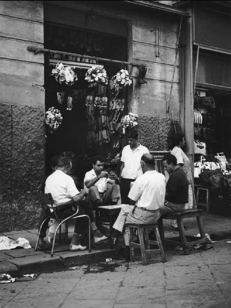 Napoli: Scene di vita varie. Napoli - Vicoli - Uomini seduti a un tavolo davanti a un negozio di scarpe - Gioco alle carte