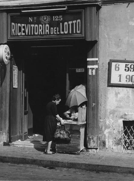 Napoli: Fortuna, fede nella fortuna. Napoli - Vicoli - Ricevitoria del Lotto - Donna davanti al banchetto - Gioco