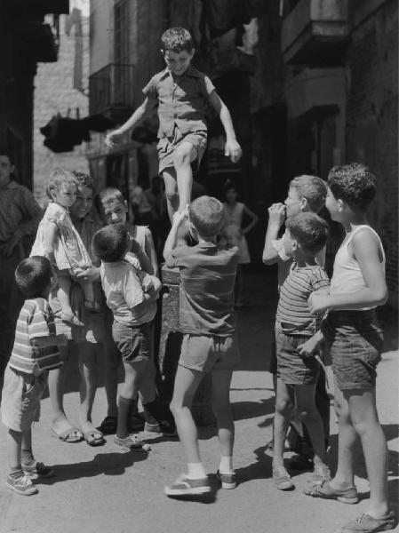 Napoli: Scugnizzi, incontri scontri. Napoli - Vicoli - Ritratto di gruppo - Bambini in cerchio al bambino sul paracarro - Gioco