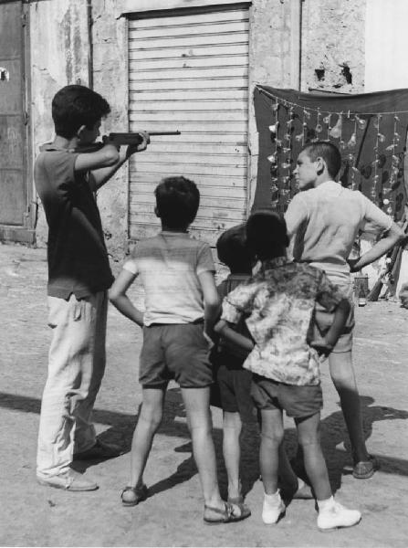 Napoli: Scugnizzi, si gioca. Napoli - Vicoli - Bambino con fucile con altri bambini - Gioco al tiro a segno