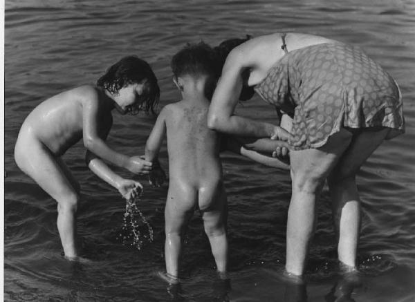Napoli: Mare/ Bimbi, soli. Napoli - Mare - Ritratto di famiglia - Donna in costume con due bambini nudi in acqua - Bagno