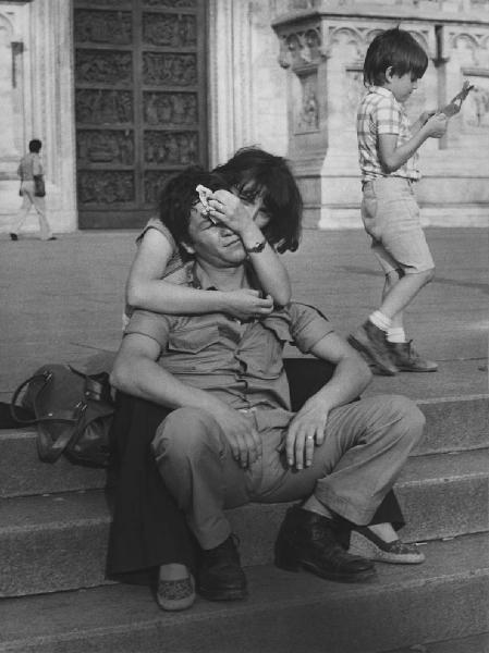 Piazza Duomo: Amore. Milano - Piazza del Duomo - Coppia di ragazzi seduti sui gradini con fazzoletto sulla faccia - Abbraccio - Bambino