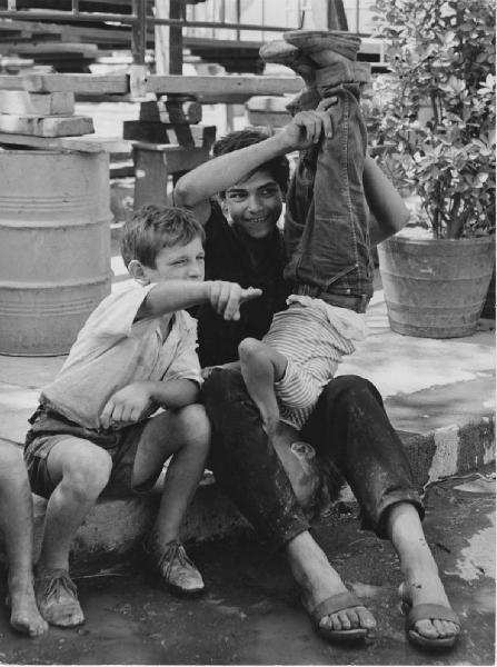 Napoli: Seconda scelta. Napoli - Esterno - Ritratto di gruppo - Tre bambini seduti su gradino di cui a testa in giù - Braccio teso