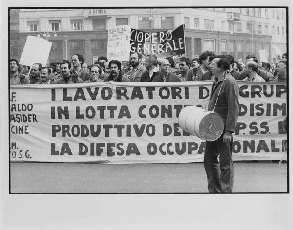 Italia: manifestazione Breda. Milano - Manifestazione operaia, sciopero generale - Corteo di operai Breda con tute da lavoro - Operaio con bidone, tamburo al collo - Striscione e cartelli di protesta contro De Mita