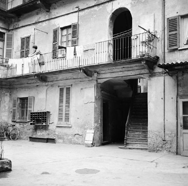 Milano - Via Abbadesse 20 - Casa di ringhiera: cortile interno - Cassette per le lettere in legno - Donna sul ballatoio che stende i panni