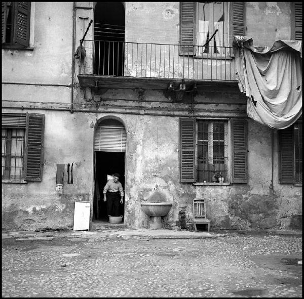 Milano - Via degli Assereto 19 - Casa di ringhiera, cortile interno - Ritratto maschile: uomo sull'ingresso di un'abitazione - Lavatoio in pietra - Panni stesi