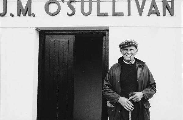 Irlanda - regione del Kerry - Sneem - mister Fitzgerald sorridente sotto un'insegna riportante la scritta "J.M. O'SULLIVAN"