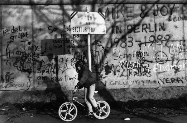 Berlino Ovest - ragazzina pedala davanti al muro - cartello con la scritta "FIN DE SECTEUR FRANCAIS"