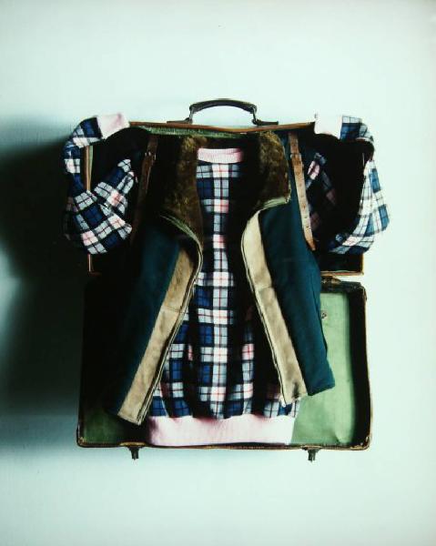 Still-life - Abiti - Valigia - Gilet in pelle e camicia scozzese piegati su valigia aperta