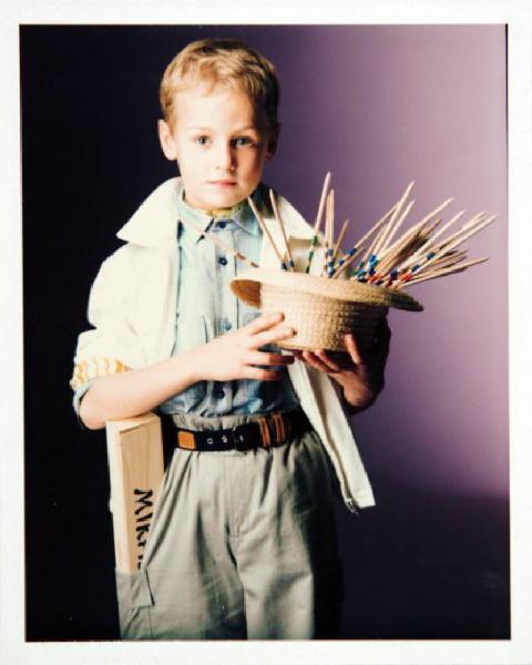 Campagna pubblicitaria per Trussardi Junior - Bambino con giubbotto bianco su camicia azzurra e pantaloni di tela - Paglietta colma di stecchini di Mikado