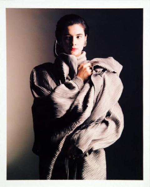 Campagna pubblicitaria per Trussardi Donna - Modella con braccia intrecciate al busto: robe-manteau di pelle plissettata grigia - Orecchini metallici
