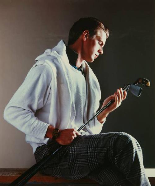 Campagna pubblicitaria per Trussardi Uomo - Sportswear - Modello seduto di profilo: girocollo di cotone bianco, pantaloni scozzesi e orologio - Due mazze da golf