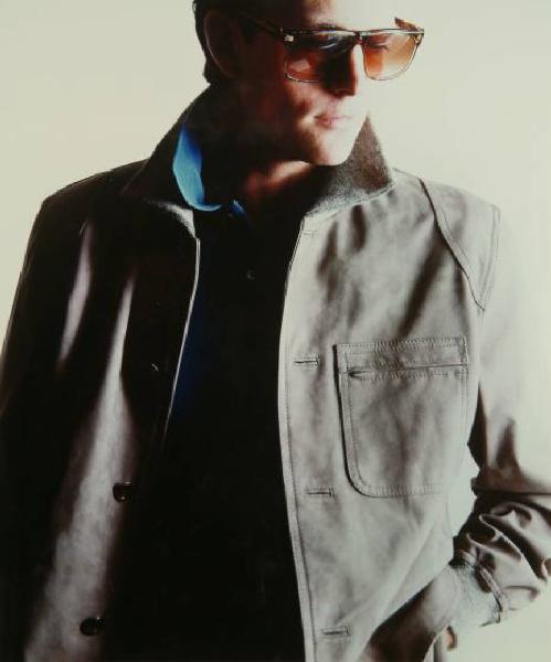 Campagna pubblicitaria per Trussardi Uomo - Modello con giacca scamosciata grigia su polo turchese e occhiali da sole