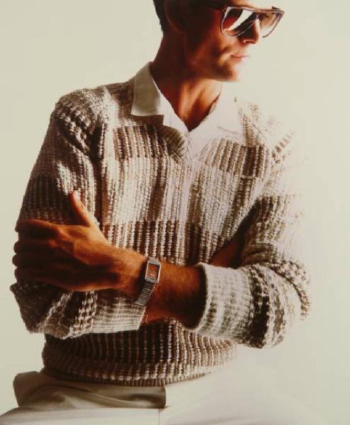 Campagna pubblicitaria per Trussardi Uomo - Modello con braccia incrociate: maglione scollato a V beige, camicia e pantaloni chiari, occhiali da sole