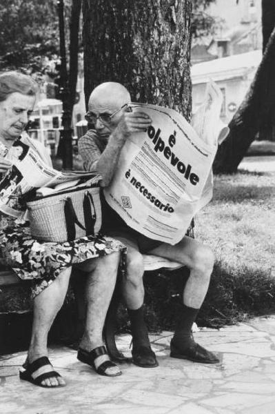 Coppia di anziani legge il giornale seduti su una panchina