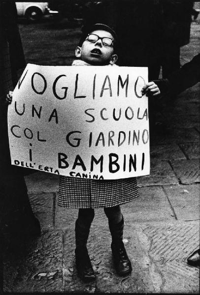Ritratto infatntile: bambino disabile sorregge un cartello con scritta "vogliamo una scuola col giardino i bambini dell'erta canina"