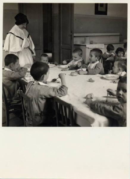 Ritratto di gruppo - Bambini a tavola con Suore di Carità / Milano - Istituto di Assistenza ai Minorenni di via Settembrini - Refettorio