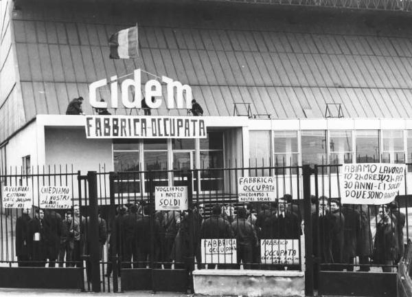Cidem - Occupazione della fabbrica - Lavoratori dietro i cancelli - Striscione e cartelli di rivendicazione - Bandiera - Insegna Cidem