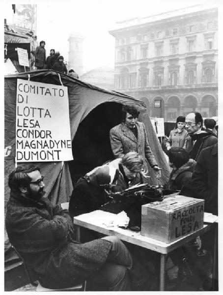 Sciopero dei lavoratori della Lesa - Presidio in piazza del Duomo - Tenda - Tavolo con macchina da scrivere e cassetta per raccolta fondi - Lavoratori - Cartelli