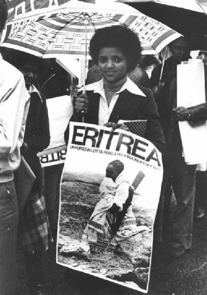 Manifestazione del primo maggio sotto la pioggia - Comizio in piazza del Duomo - Ritratto femminile - Donna eritrea con cartello