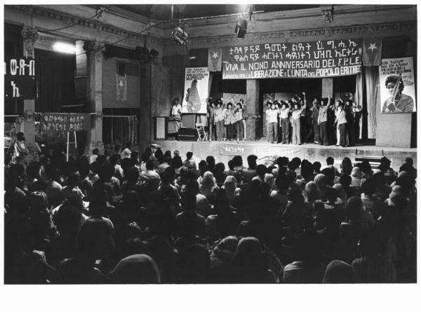 IX anniversario della fondazione del Fple - Interno - Manifestazione per la liberazione e l'unità del popolo eritreo - Palco - Coro di donne e uomini eritrei salutano con il pugno chiuso - Parola d'ordine - Bandiera - Manifesto