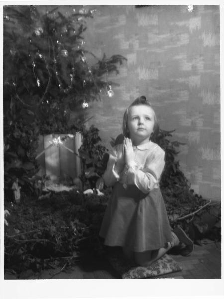 Ritratto infantile. Monti. Bambina in preghiera / Festa - albero di Natale - presepio
