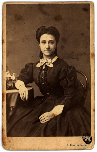 Ritratto femminile - Donna in abito scuro seduta accanto a un tavolo
