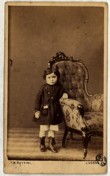 Ritratto infantile - Bambina in piedi accanto a una poltrona