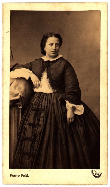 Ritratto femminile - Donna in giacca e gonna scura, in piedi con il braccio destro appoggiato a un piedistallo