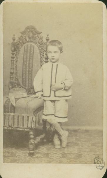 Ritratto infantile - Bambino in piedi accanto a una poltrona