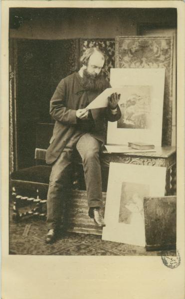 Ritratto maschile - Elmon, seduto su un tavolo, accanto a due opere pittoriche e con un foglio in mano