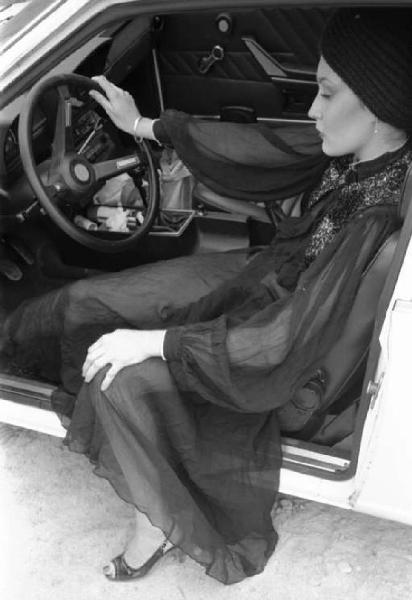 Ritratto femminile - giovane - modella seduta all'interno dell'abitacolo di un'automobile e che indossa un abito lungo a veli e turbante in testa