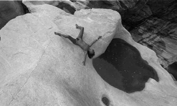 Nudo femminile - modella sdraiata su rocce vicino a una pozza d'acqua