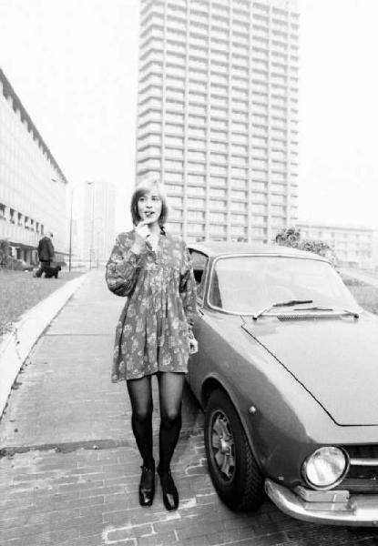 Ritratto femminile - modella con auto e passante tra palazzi per uffici