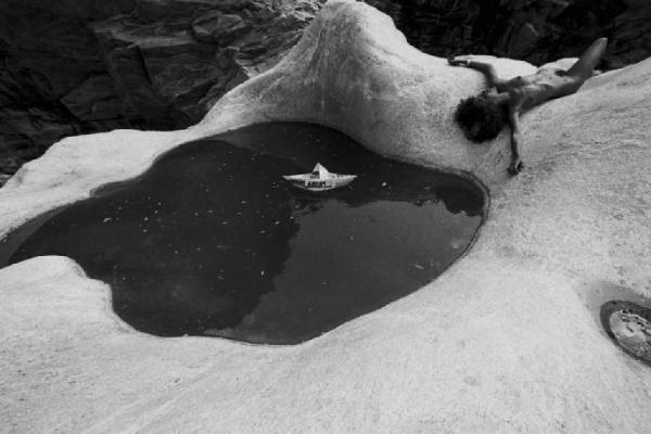 Modella nuda accanto a pozza d'acqua, sdraiata su rocce sagomate da un torrente