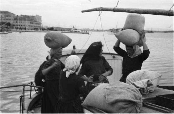 Viaggio in Jugoslavia. Sebenico: un gruppo di contadine carica la merce appena acquistata sulle proprie imbarcazioni