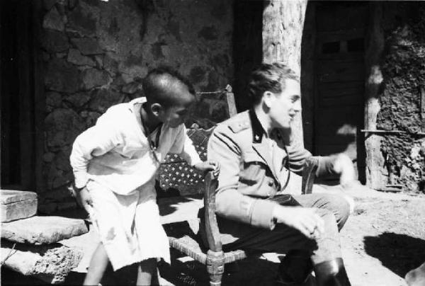 Viaggio in Africa. Insediamento indigeno di Mai Otza - soldato italiano seduto si riposa - al suo fianco un fanciullo indigeno