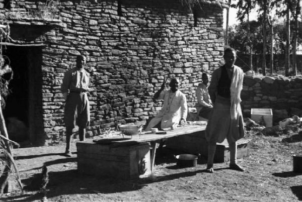 Viaggio in Africa. Militari indigeni durante la preparazione del pranzo nei pressi di un edificio in pietra