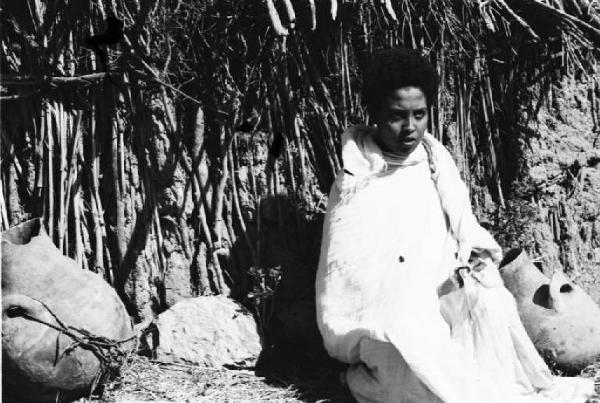 Viaggio in Africa. Ritratto femminile - una donna indigena sulla soglia della sua capanna. Accanto a lei vi sono delle anfore in cotto